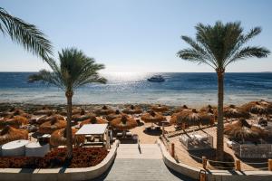 a beach with palm trees and a boat in the water at Sunrise Remal Beach Resort in Sharm El Sheikh