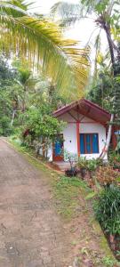 a small white house with blue windows and a dirt road at Rainforest Soul Villa in Mederipitiya
