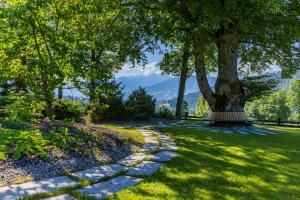 a park with a tree and a bench in the grass at Hotel Ramsauhof Zimmer Appartement Pool & Wellness in Ramsau am Dachstein +114 photos