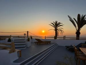 a sunset on the beach with benches and palm trees at Dimael Mansion in Fira