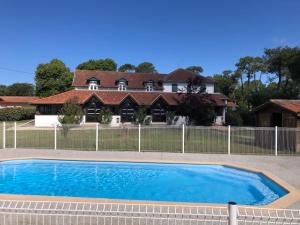 a house with a swimming pool in front of a fence at Hôtel La Chaumière-Les Pastourelles in Capbreton