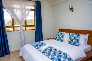 a bedroom with a bed with blue curtains and a window at Sai Inn Eldoret in Eldoret