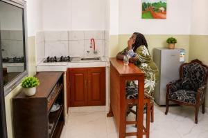 a woman sitting at a table in a kitchen at TCHASSHOUSE Motel in Yaoundé