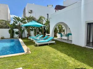 a group of lounge chairs with an umbrella and a pool at Villa Sky in Bin Rhilouf