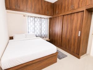 a bedroom with a white bed and wooden cabinets at SV Serviced Apartments in Chikmagalūr