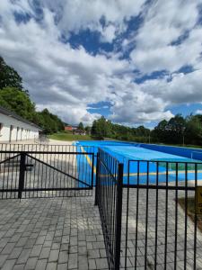 a blue pool behind a fence with a cloudy sky at Sowi Zakątek in Jugów