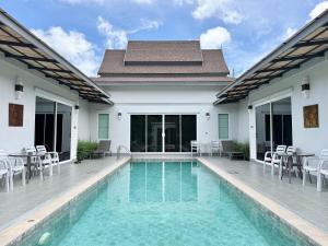a swimming pool with chairs and tables and a house at Phuket La Siesta, Naiharn Beach in Nai Harn Beach