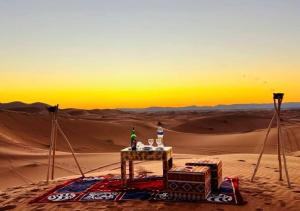 a table in the middle of the desert at sunset at Amazing Luxury Camp in Merzouga