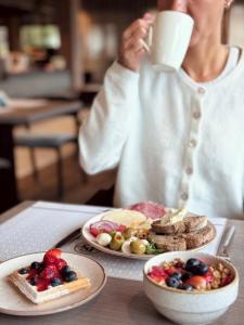 a woman drinking a cup of coffee next to plates of food at Hotel Litworowy Staw in Białka Tatrzańska