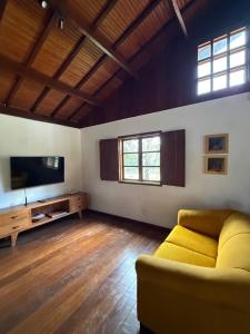 a living room with a yellow couch and a flat screen tv at Casa Sol Piscina e Cachoeira in Pirenópolis
