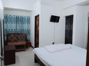 a bedroom with a bed and a chair and a television at Rifaee Cox Palace in Cox's Bazar