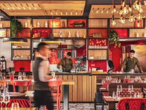 a man walking through a restaurant with two men preparing food at Novotel Paris Vaugirard Montparnasse in Paris
