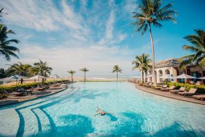 a person swimming in a pool at a resort with palm trees at Devasom Khao Lak Beach Resort & Villas in Khao Lak