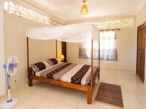 a bedroom with a canopy bed and a fan at Appartement Baie-Rose SP Nosy-Be in Nosy Be