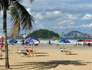 a beach with chairs and umbrellas and the ocean at Flat São Vicente Praia Piscina Garagem in São Vicente