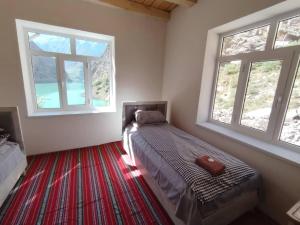 a bedroom with a bed with two windows and a red carpet at Nofin Lake House in Panjakent