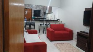 a living room with two red chairs and a kitchen at Casa com varanda, garagem e cozinha completa in Formosa