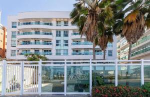 a large white building with palm trees in front of it at FLAT MANDAI PREMIUM - Cabo Frio in Cabo Frio