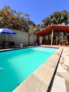 a blue swimming pool with an umbrella and a patio at Chácara buriti in Pirenópolis