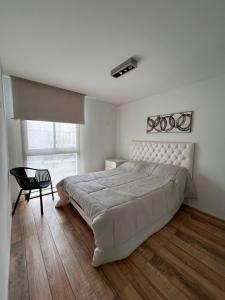 a white bedroom with a large bed and a chair at Emma in Villa Carlos Paz