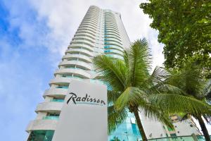 a tall building with a sign in front of a palm tree at Hotel Beira Mar Boa Viagem By Flatbpaiva in Recife
