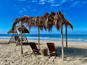 two chairs and a straw hut on a beach at Nativo Lodge in Playas