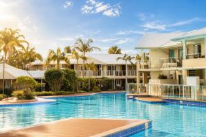 a resort swimming pool with palm trees in the background at Luxury Renovated Resort Studio Apartment - Oaks Pacific Blue in Salamander Bay