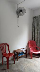 a room with a red chair and a table and a fan at Ilham inn in Jerantut