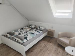 a white bedroom with a bed and a chair at Dömper Döme Apartman in Balatonlelle