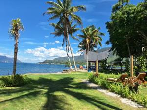 a park with palm trees and a house next to the water at Pondok Ganda in Ambarita