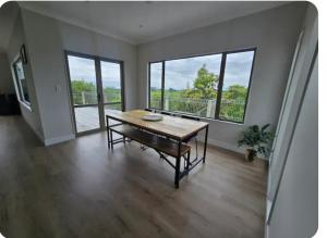 a dining room with a table and large windows at Casa Del Sol in Riwaka