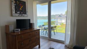 a living room with a television on a dresser with a view of a patio at Hermitage Apartment E03B - Seeblick & Zugang in Maria Wörth