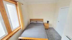 a small bedroom with a bed and two windows at Stornoway Stays Apartment in Stornoway