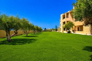a green yard with trees and a building at Golden Bay Apartments-Garden Haven in Malia