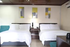two beds in a hotel room with white sheets at The Stafford Lodge in Freetown