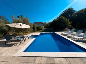 a swimming pool with chairs and an umbrella at Holiday Home Slap Koćuša in Ljubuški