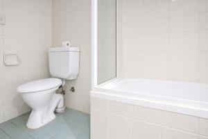 a white bathroom with a toilet and a bath tub at 2 Bedroom House Woolloomooloo in Sydney