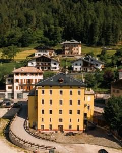 a large yellow building on a hill with houses at Càdor Hotel in Valle di Cadore