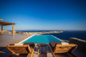 a pool with chairs and a table and the ocean at Birdhouse Private Luxury Villa in Agios Ioannis Mykonos