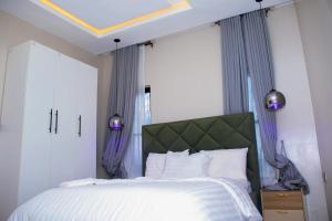 a bedroom with a bed with a green headboard and purple curtains at Dream Nest in Benin City +18 photos