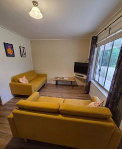 a living room with two yellow couches and a television at Restaway Holiday Units in Porepunkah