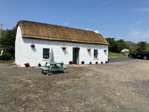 a white building with a grass roof with a picnic table at Anne’s Thatched Cottage in Kilcar