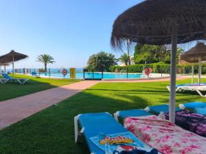 a row of beach chairs and an umbrella on the grass at Calma Bungalow 54b en Urbanización La Roca in Torremolinos