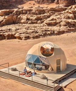 a dome tent in the desert with people sitting in it at camp sand in Disah