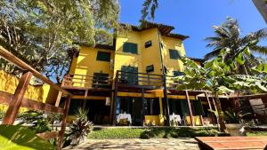 a large yellow building with chairs and trees at Pousada Oceanica Buzios in Búzios