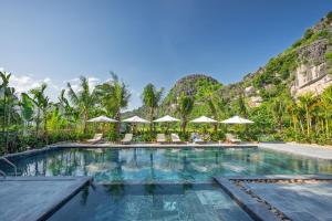a swimming pool with chairs and umbrellas in front of a mountain at Hang Múa Ecolodge Ninh Hoà in Ninh Binh