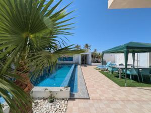 a swimming pool next to a house with a palm tree at Villa SUN SQUARE DJERBA in Awlād ‘Umar