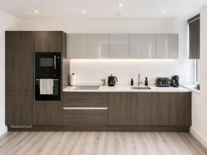 a kitchen with wooden cabinets and a black refrigerator at Luxury Central Solihull Apt - King Bed, Sofa Bed & 2 Parking Spaces in Solihull