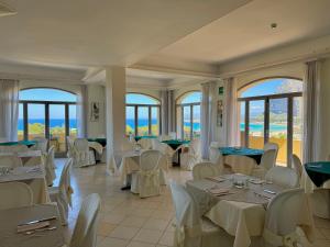 a restaurant with white tables and chairs and windows at Hotel Panoramic in San Vito lo Capo