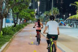two people riding bikes down a sidewalk at night at Pousada Vila Taquaras in Balneário Camboriú